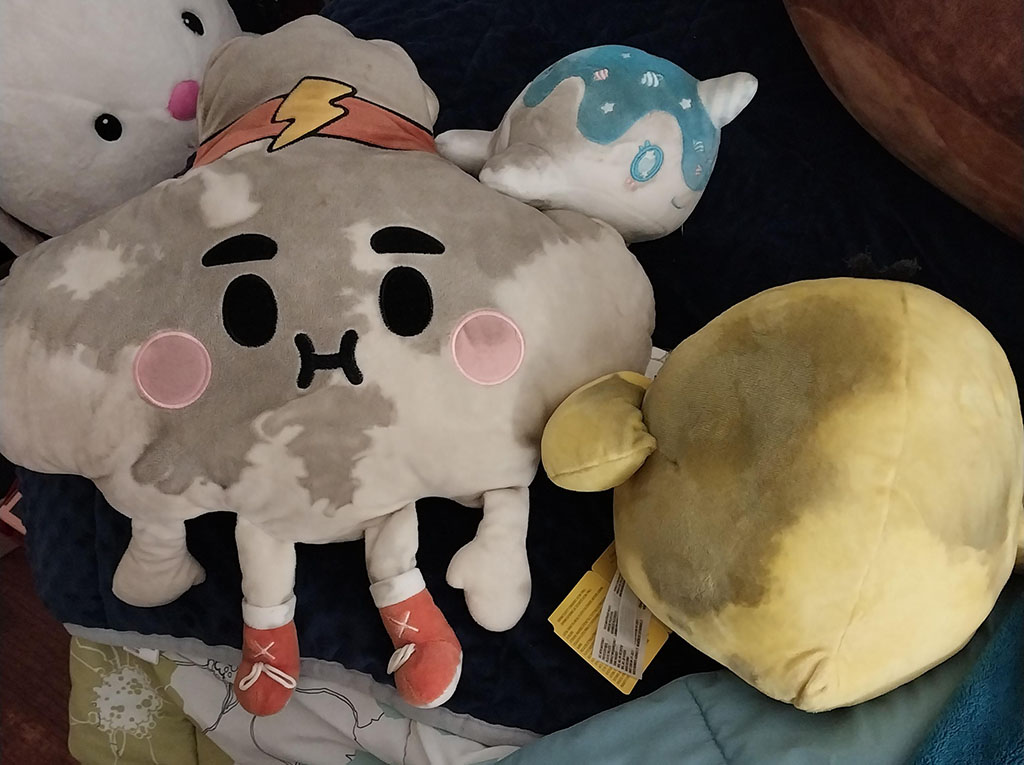 Group of plush toys showing dark discoloration and blackish patches on the fabric surface, indicating possible mold or moisture damage.