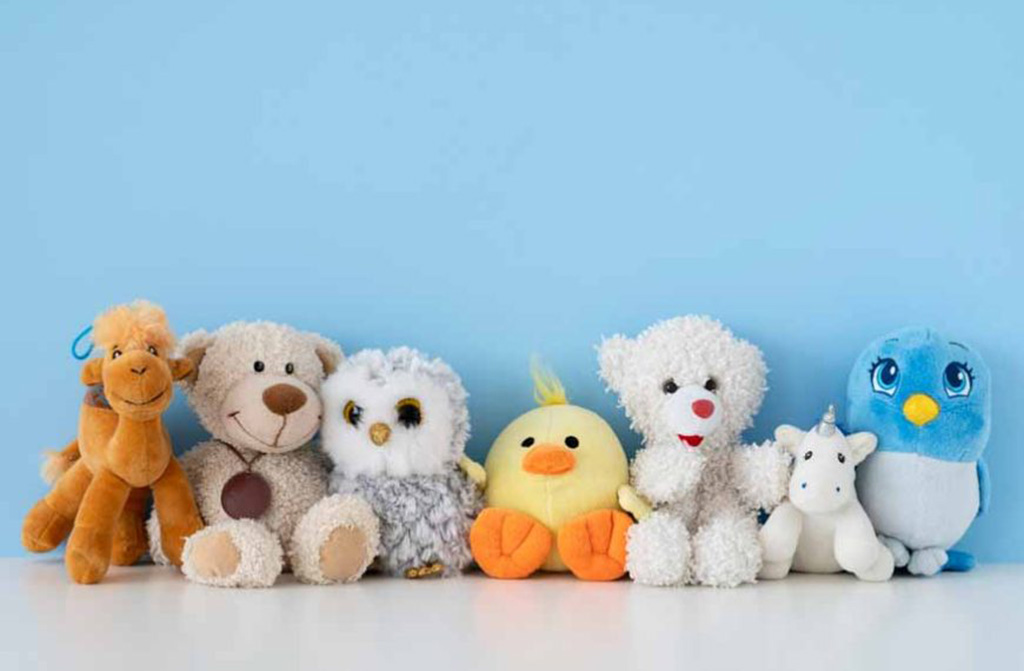 A lineup of cute plush toys including a camel, bear, owl, chick, white teddy, unicorn, and blue penguin arranged against a light blue background.