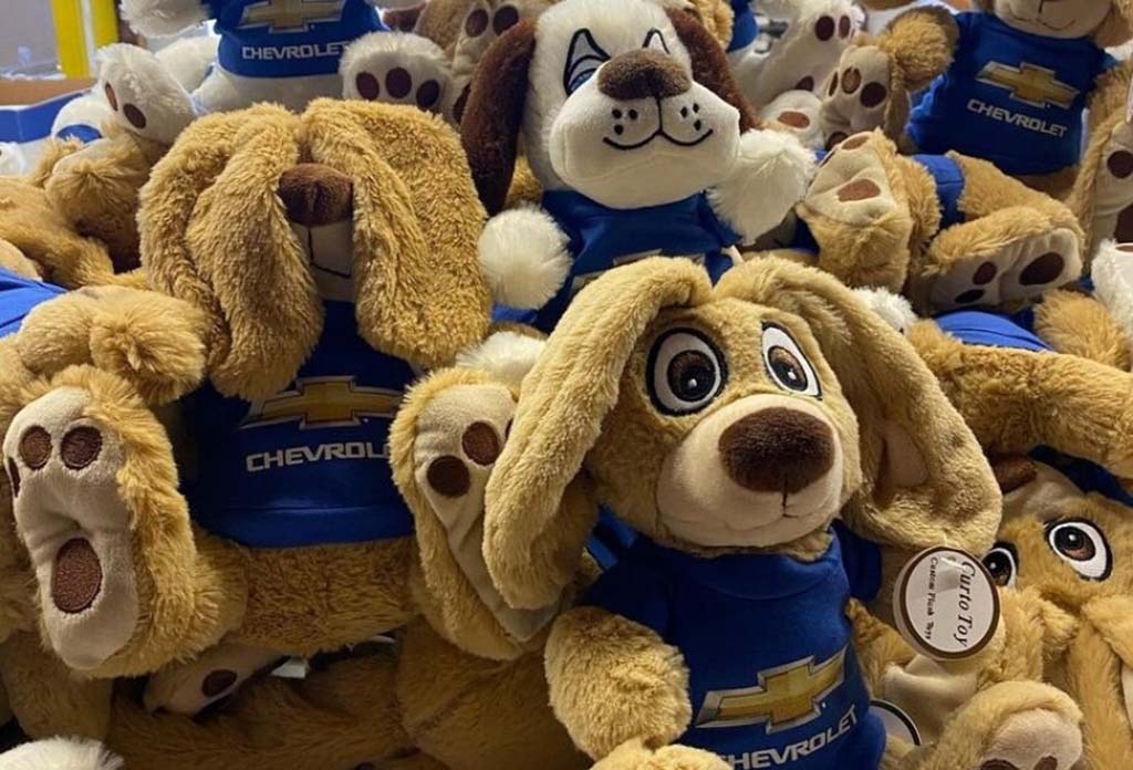A pile of brown plush dog toys wearing blue Chevrolet logo shirts displayed together.