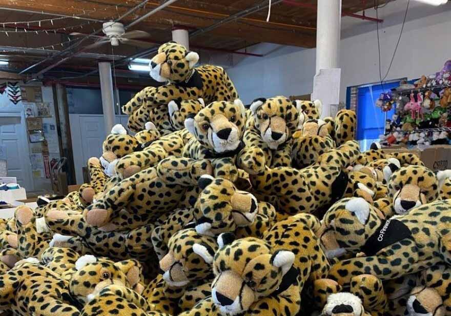 A large pile of plush cheetah stuffed animals stacked in a warehouse or storage room, showing numerous identical spotted toys prepared for distribution.