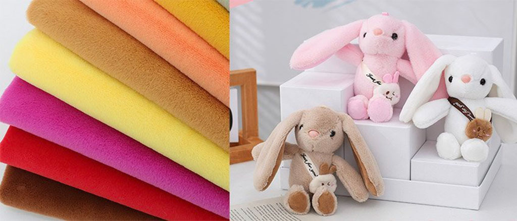 Stack of colorful fleece plush fabrics beside three handmade bunny plush toys made from the same soft material.