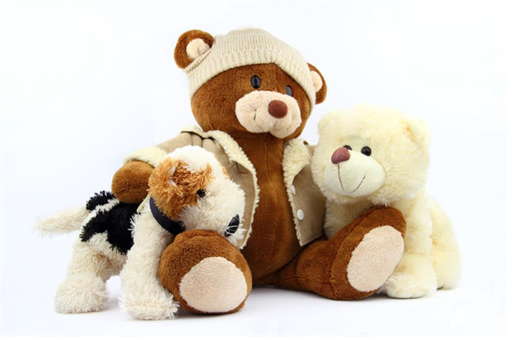 Group of soft plush toys including a brown teddy bear in a jacket and beanie, a small white bear, and a plush dog, displayed on a white background.