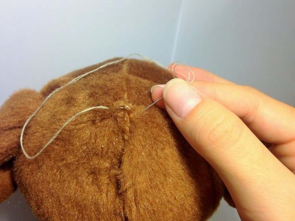 Close-up of hands sewing a brown stuffed animal with a needle and thread.