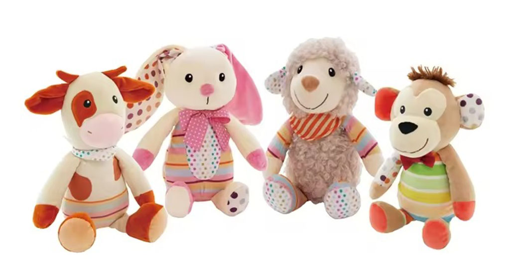 Four colorful stuffed animals—a cow, bunny, lamb, and monkey—sitting in a row with patterned fabric details.