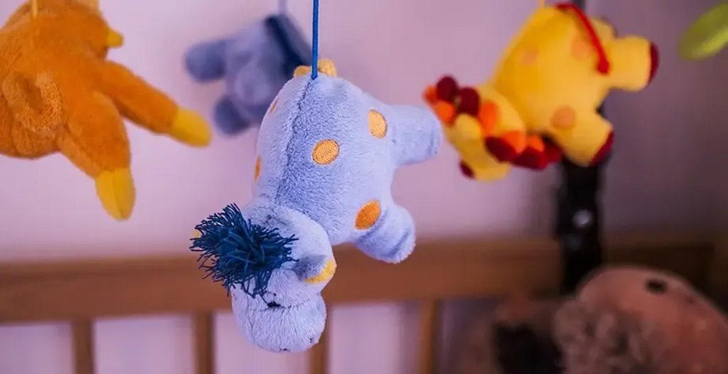 Soft blue plush animal with orange spots hanging from a baby mobile, surrounded by other colorful stuffed animals.