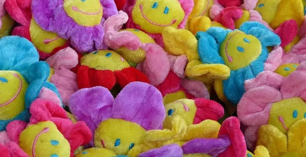 Pile of bright plush flower toys with smiling faces in pink, yellow, blue, and purple colors.