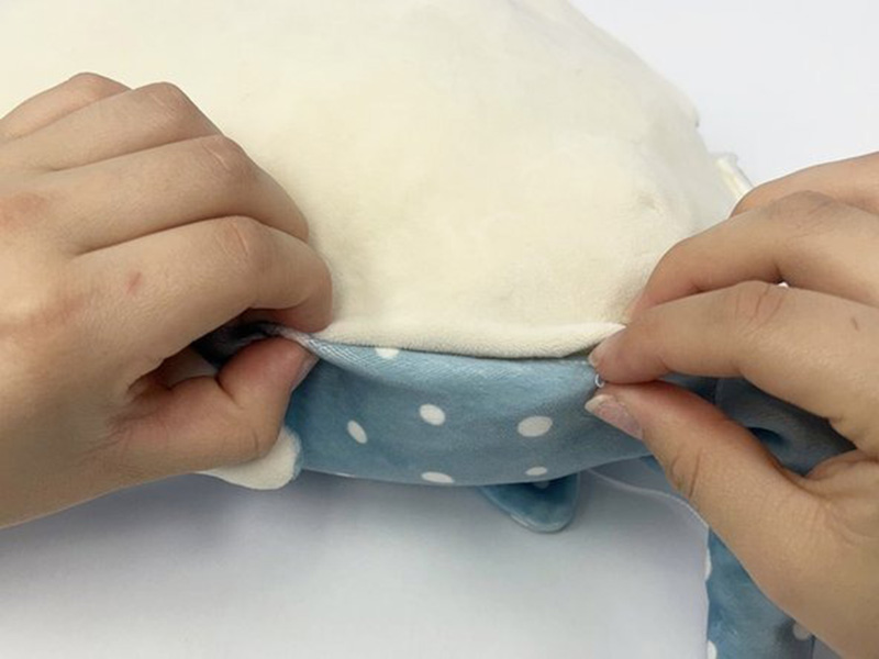 Hands gently closing and stitching a plush toy seam, showing the final step of repairing a soft stuffed animal.