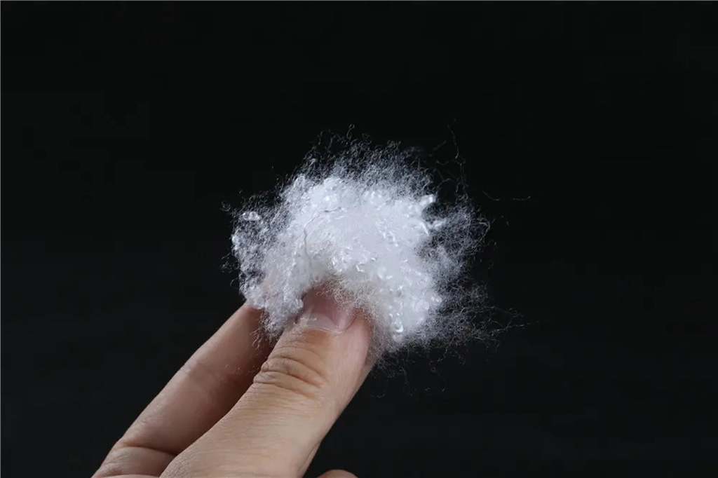Close-up of a hand holding a small cluster of white polyester fiberfill, showing fine texture and softness used for plush toy and pillow stuffing.