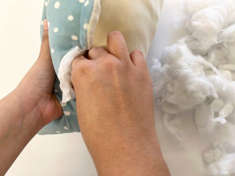 Hands adding fresh polyester fiberfill into a plush toy through an open seam during a repair or restuffing process.