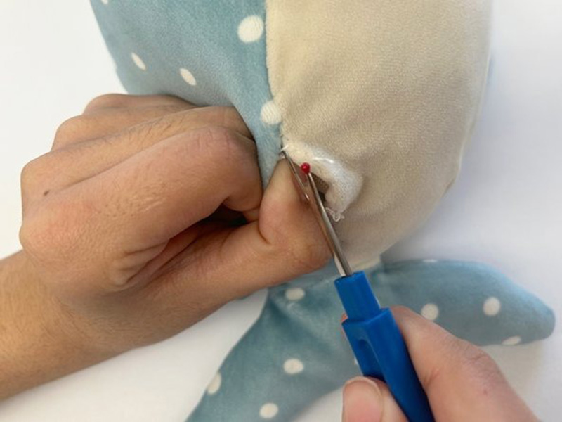 Close-up of hands using a seam ripper to carefully open a stitched seam on a plush toy for repair or restuffing.
