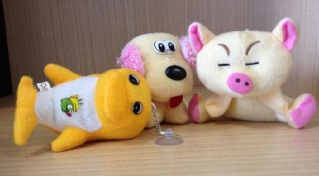 Three small plush toys including a yellow fish, beige dog, and pink-eared pig displayed on a wooden surface.