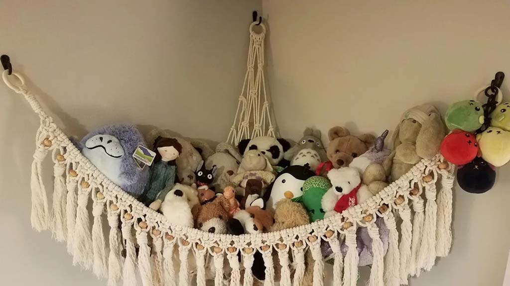 Macrame-style stuffed animal hammock filled with various plush toys hanging on wall.