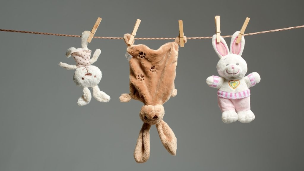 Three plush bunny toys hanging on a clothesline with clothespins, drying after cleaning.