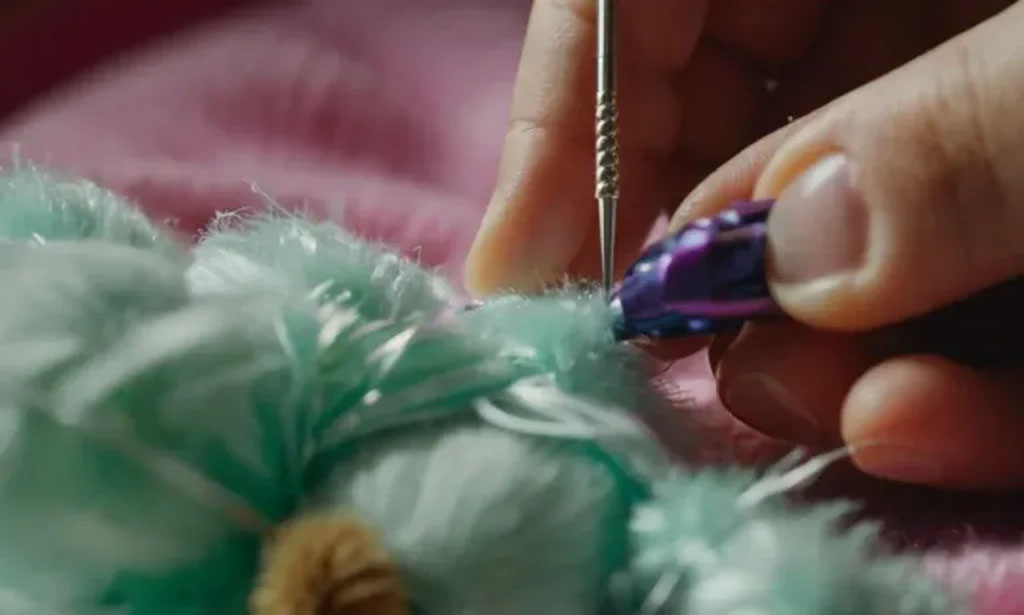 Close-up of hands sewing a hole in a fluffy mint-green stuffed animal using a needle and thread.