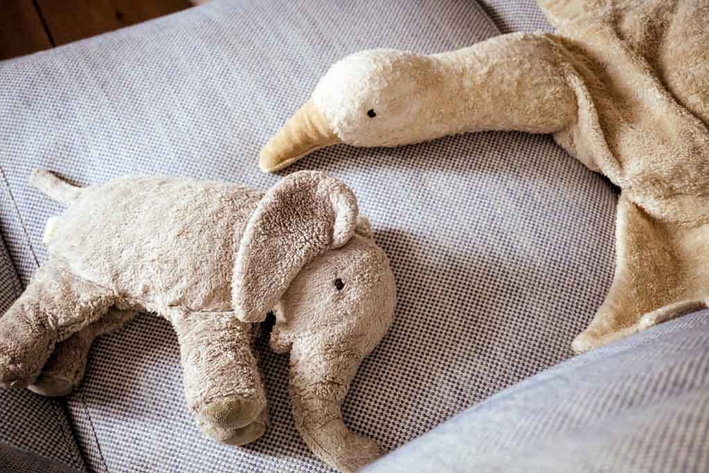 Beige plush elephant and goose toys resting on a fabric sofa, showing their soft, cuddly texture and gentle neutral colors.