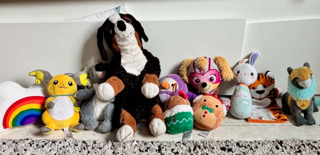 Group of colorful plush toys including animals and characters arranged on a floor, showing various fabric textures and vibrant designs used in soft toy manufacturing.