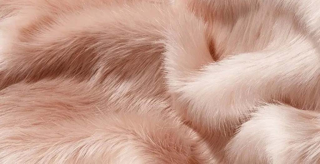  Close-up of fluffy light pink faux fur fabric, showing smooth and dense fibers ideal for plush toys and luxury stuffed animals.
