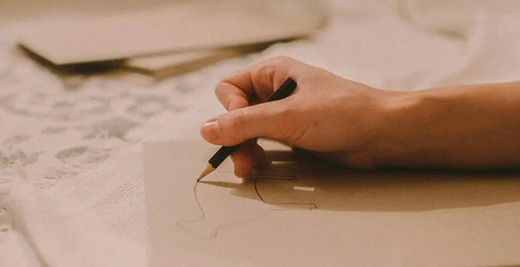 Close-up of a person drawing a simple character sketch on paper, representing the first step of turning artwork into a custom plush toy.