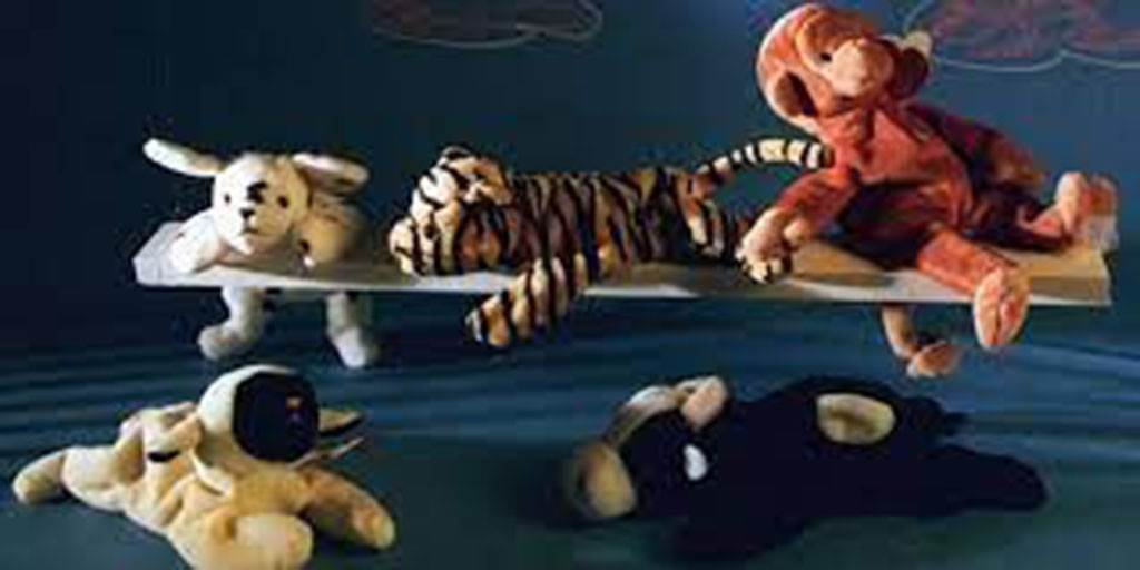 Five vintage Beanie Baby–style plush animals posed together on a blue surface, including a dog, tiger, monkey, lamb, and cow