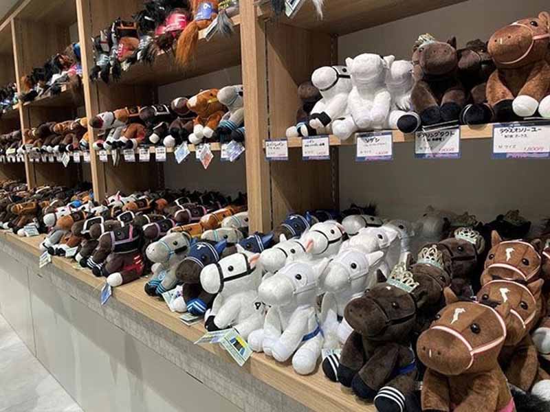 A large display of plush horse toys arranged on wooden shelves, showing various colors and saddle designs in a retail store setting.