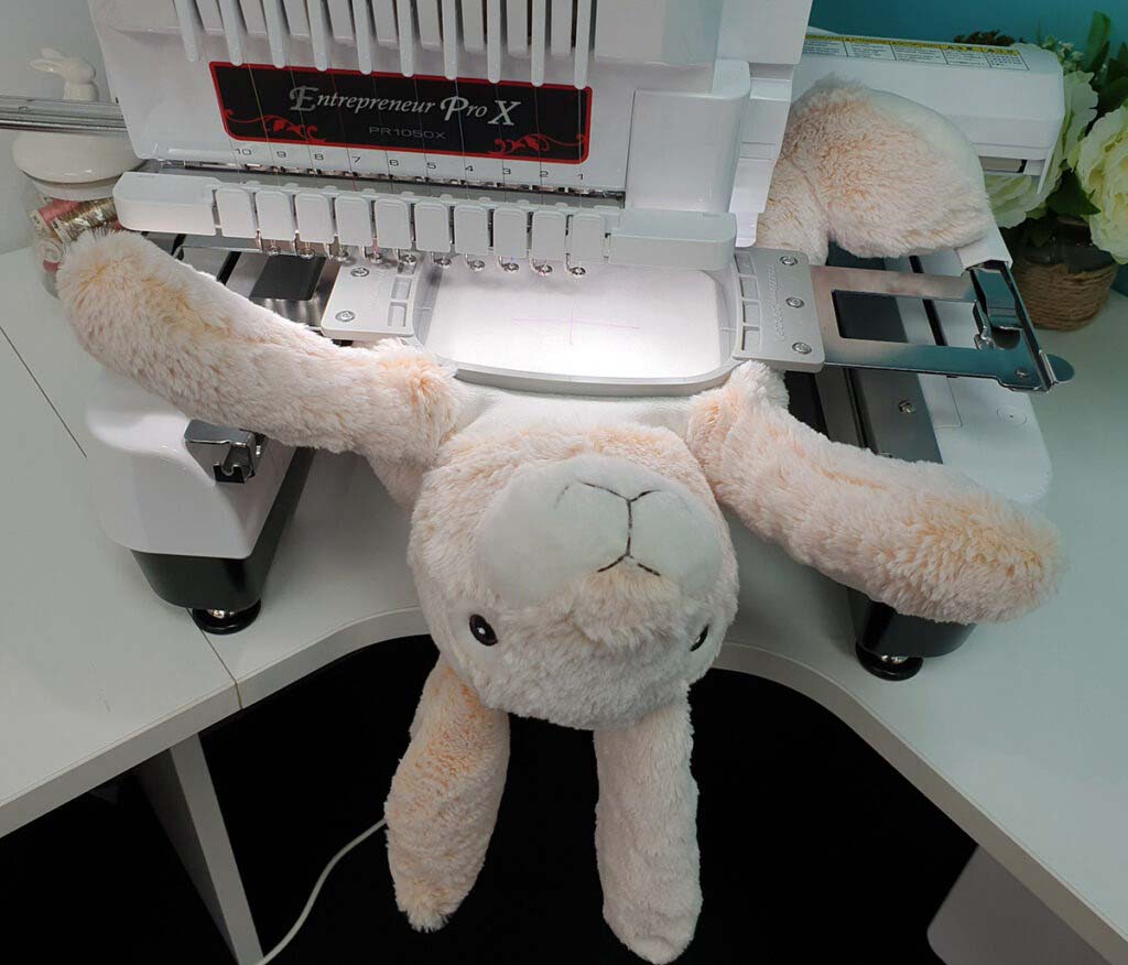 A plush bunny positioned on an embroidery machine, prepared for stitching or customization work.