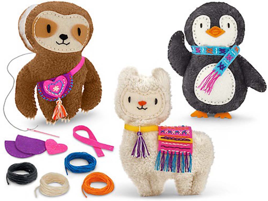 A set of handmade plush animals—including a sloth, llama, and penguin—decorated with felt accessories, colorful threads, and craft materials displayed beside them.