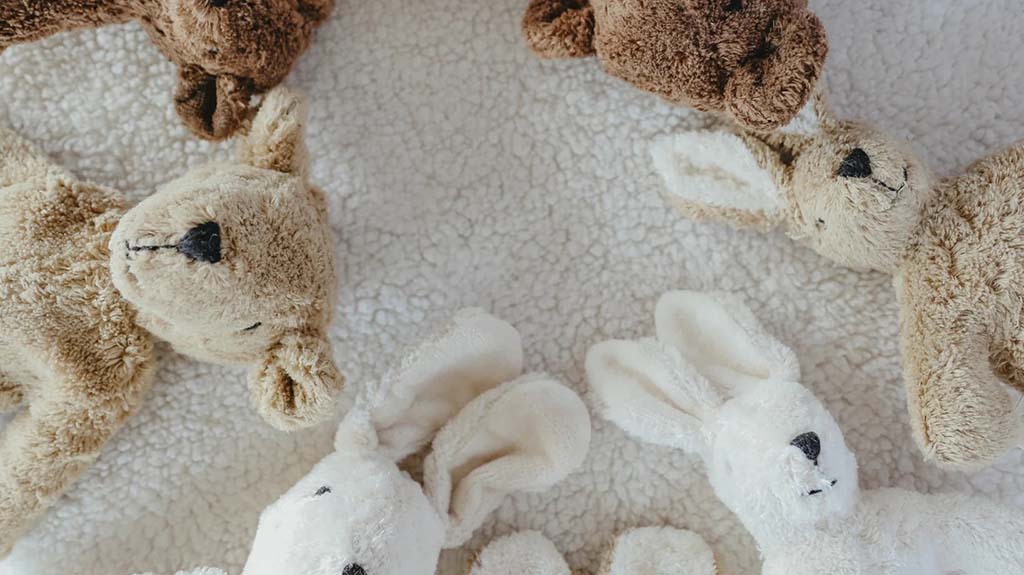  A cozy arrangement of plush bears and rabbits in beige, brown, and white tones placed in a circle on a soft textured blanket.