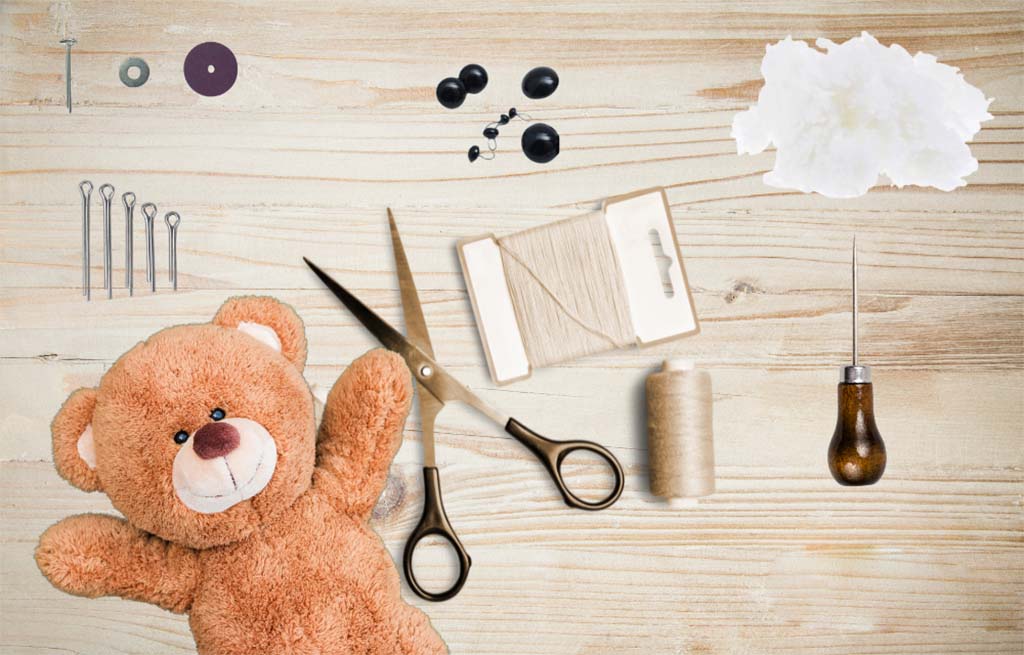Flat lay of teddy bear making tools and materials including scissors, needles, thread, stuffing, and toy eyes on a wooden surface with a plush bear.
