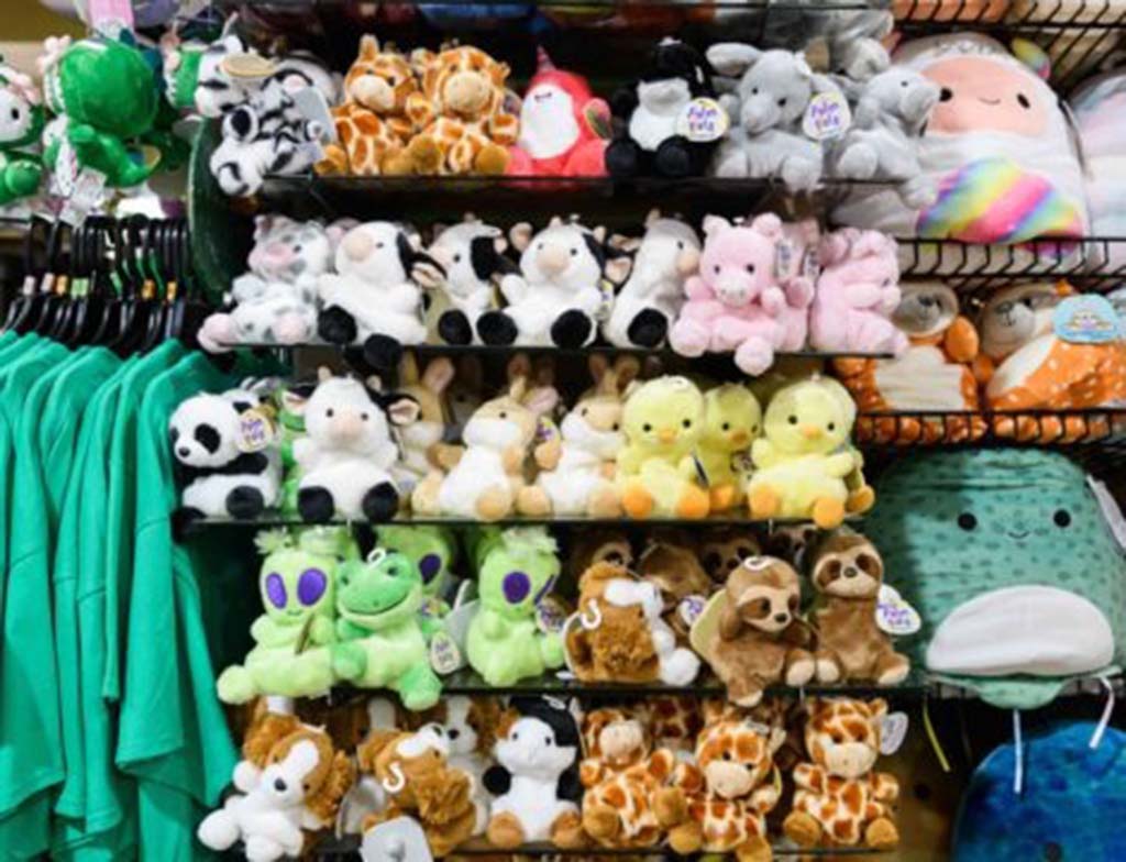 Shelves filled with colorful plush animals including cows, giraffes, ducks, pandas, and frogs in a toy store display.