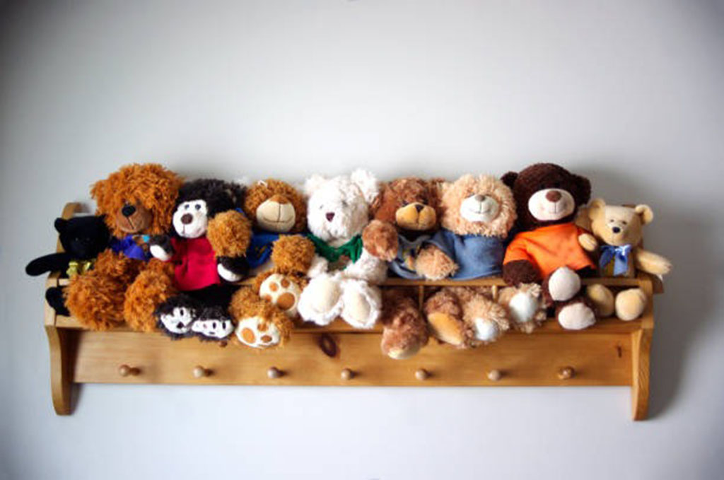 A wooden wall-mounted shelf neatly lined with various plush teddy bears and stuffed animals, all sitting close together in a row.