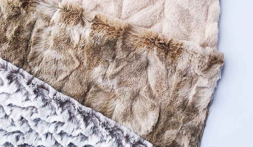 Close-up of layered faux fur fabric samples in beige, brown, and white tones, showcasing soft textures and realistic patterns used for plush toys.