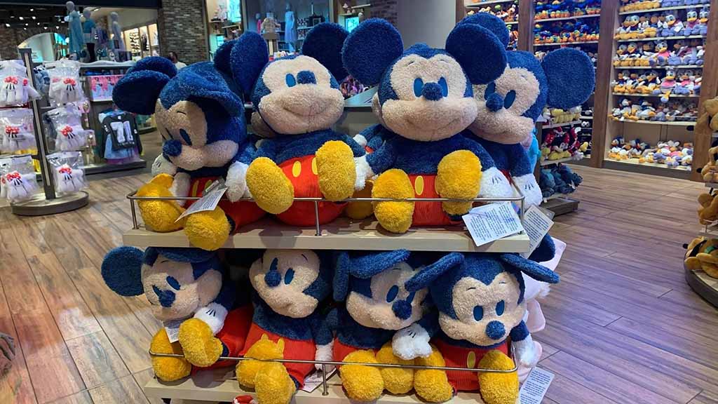  Rows of blue and red Mickey Mouse plush toys neatly arranged on shelves inside a Disney retail store.