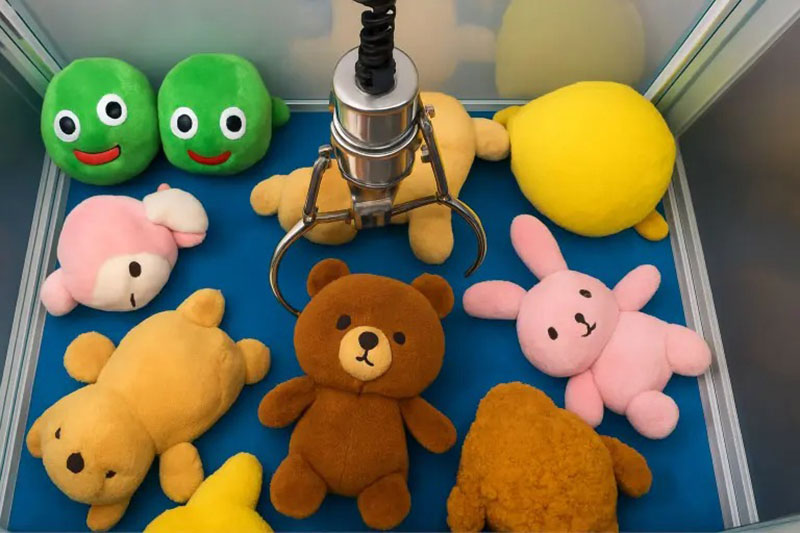 A claw machine filled with colorful plush toys, including bears, bunnies, and green round characters, with the claw positioned above them.