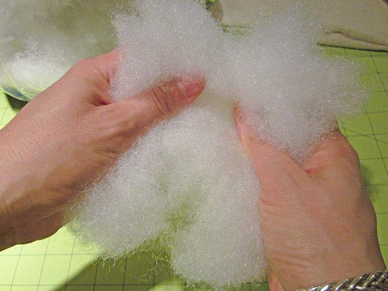 Two hands pulling apart fluffy white polyester fiberfill used for stuffing plush toys.