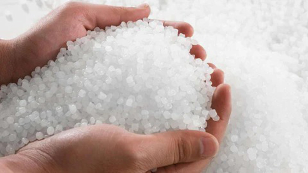 Hands holding small white plastic pellets used as stuffing material for weighted plush toys.