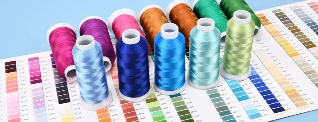 Multiple vibrant embroidery thread spools arranged on top of matching color reference charts for fabric and sewing design selection.