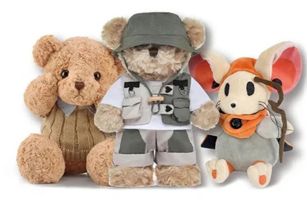 Three plush toys displayed side by side: a soft brown teddy bear in a knitted vest, a teddy bear wearing a green bucket hat and explorer outfit, and a mouse plush with large pink ears and an orange scarf.