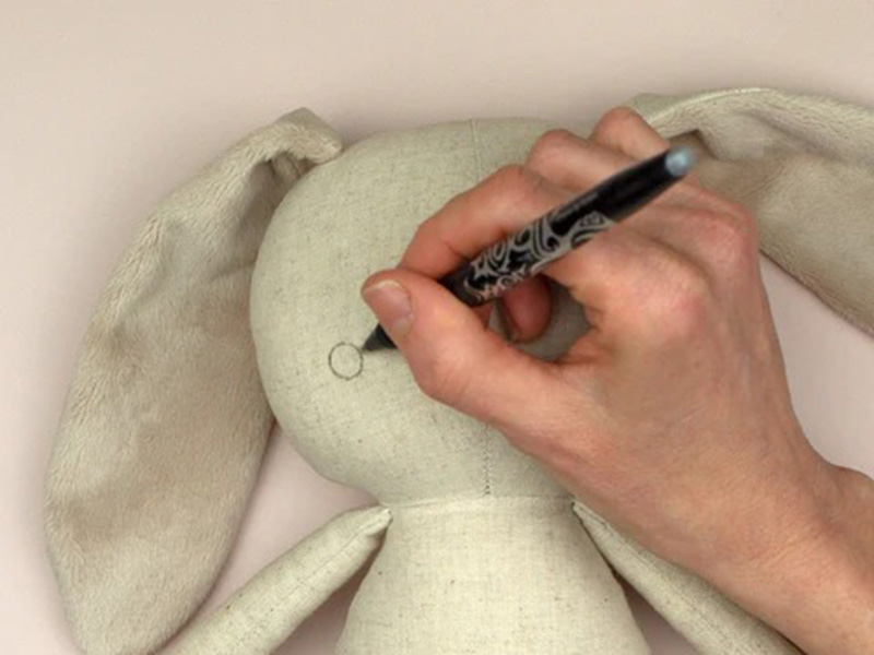 Hand drawing eye circle on fabric doll head using a fabric marker.