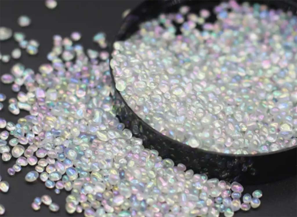 Close-up of shimmering iridescent poly beads scattered around a black container, commonly used for weighting plush toys.
