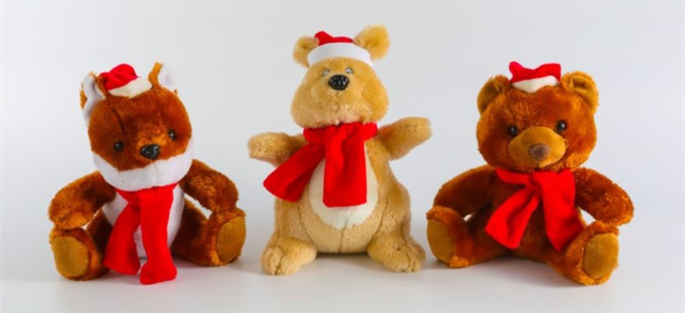 Three plush stuffed animals wearing red Christmas scarves and Santa hats, including a fox, a beige bear, and a brown bear, displayed against a plain white background.
