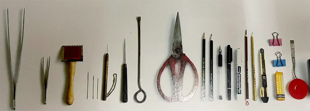 A neatly arranged row of plush-toy making tools including long tweezers, brushes, needles, scissors, markers, pencils, cutters, clips, and measuring tape displayed on a white surface.