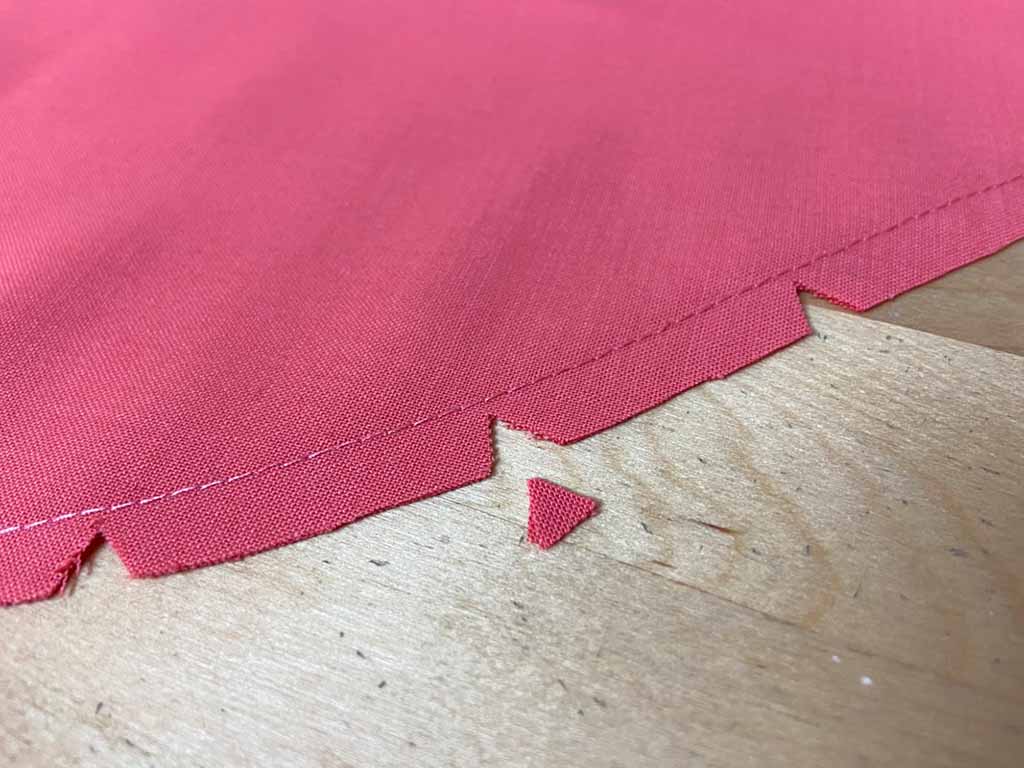 Close-up of pink fabric with small V-shaped notches cut along the seam allowance to help the curved seam lie flat after turning.