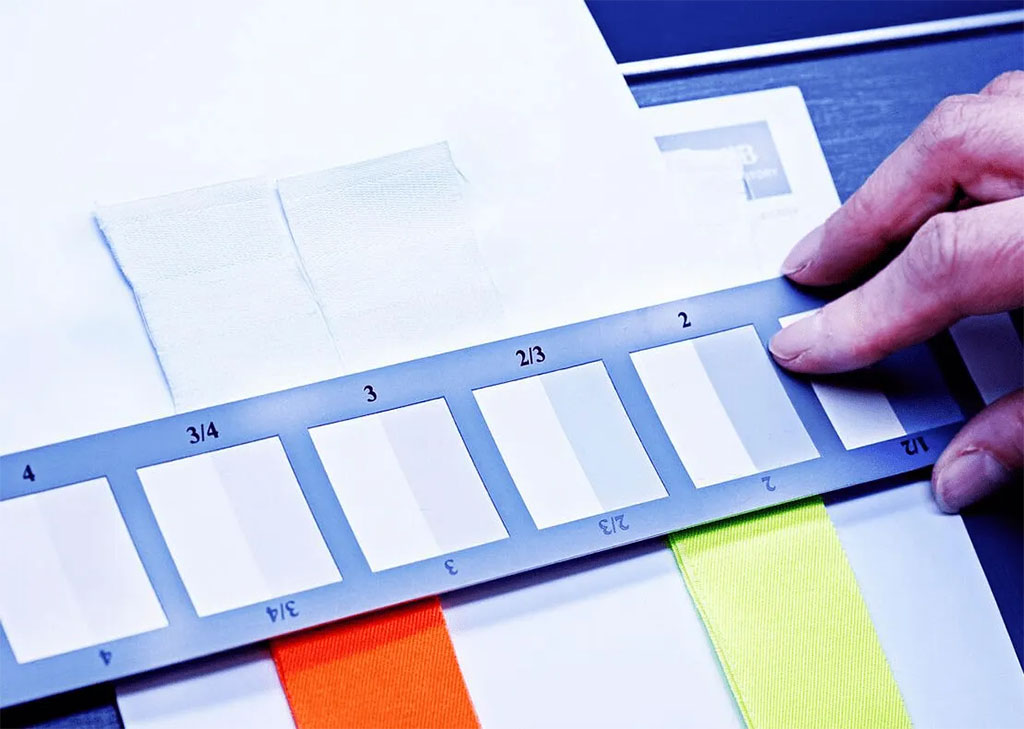Close-up of a technician using a gray scale card to evaluate fabric colorfastness, comparing shade changes on textile samples to ensure high-standard quality and safety compliance.