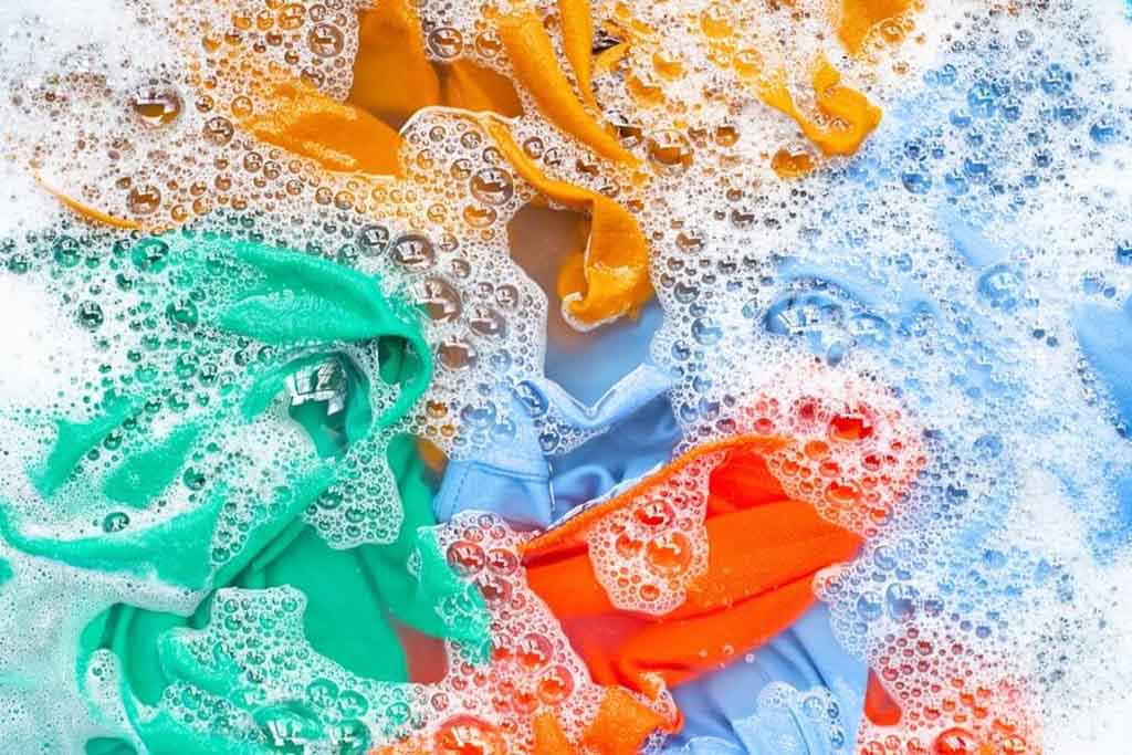 Colorful fabric pieces soaking in soapy water with foam and bubbles during hand washing.