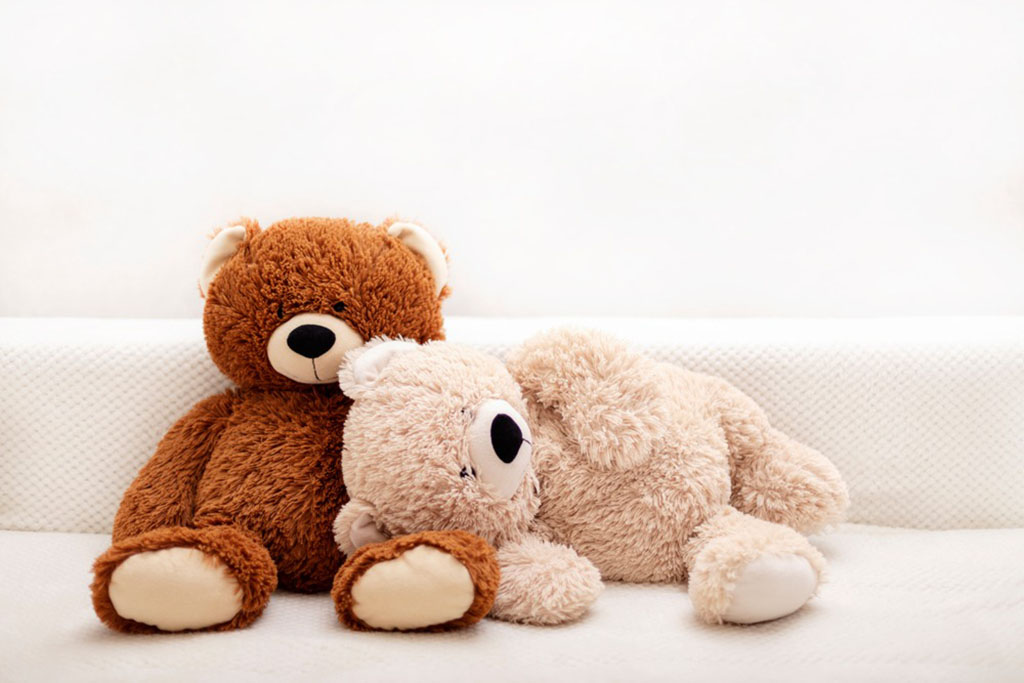 Two soft teddy bears, one brown and one beige, sitting and lying together on a white textured surface.