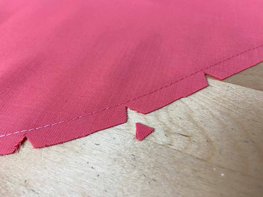 Close-up photo of pink fabric with small V-shaped seam-allowance notches cut along the stitched edge to help curves turn smoothly in plush toy sewing.