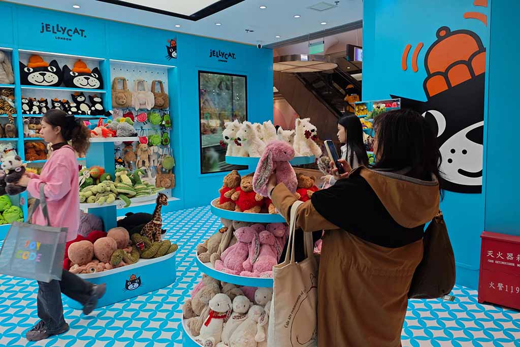 Customers browsing and photographing plush toys inside a brightly decorated Jellycat store, with shelves full of stuffed animals and colorful displays.