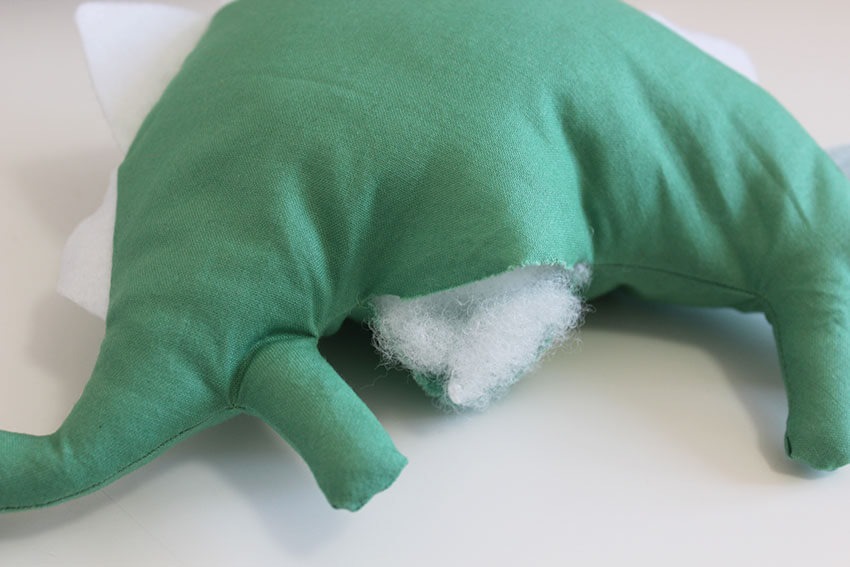 Stuffed toy with green fabric showing ripped seam and white stuffing coming out.