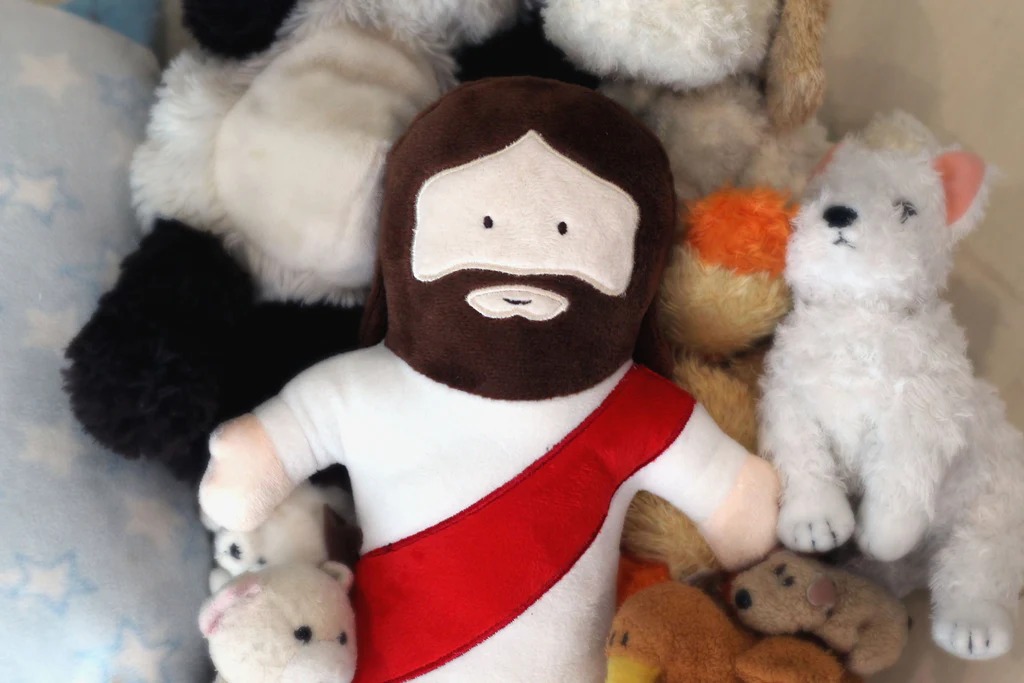 A group of plush toys arranged together, featuring a distinctive plush figure with a beard and red sash among various animal plushies.