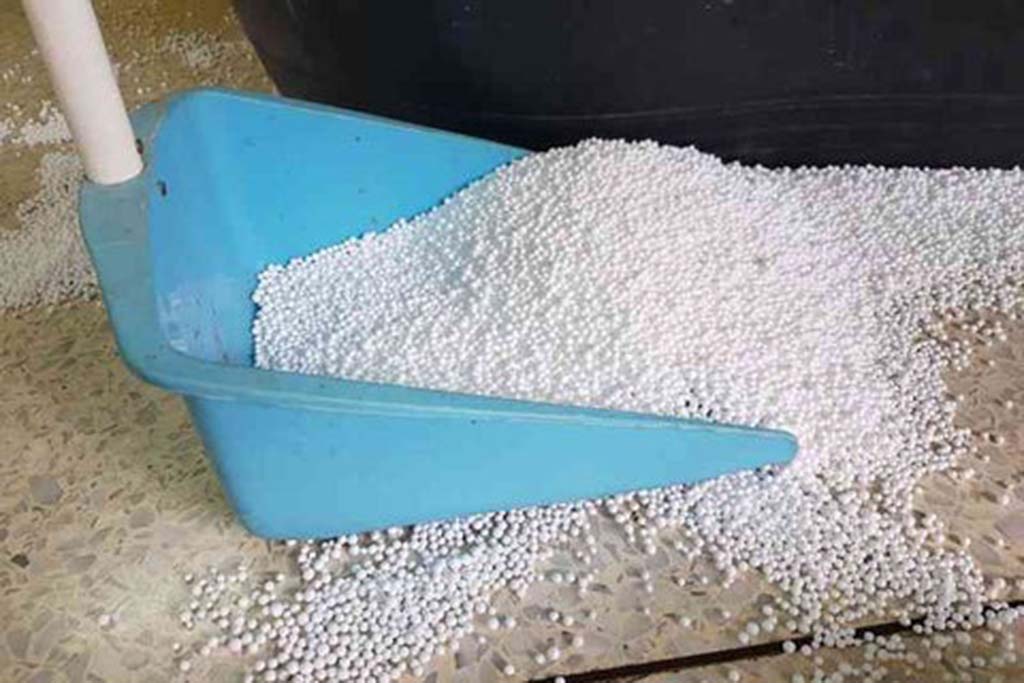 White plastic poly pellet beads being collected in a blue dustpan, commonly used as filling for weighted stuffed animals.
